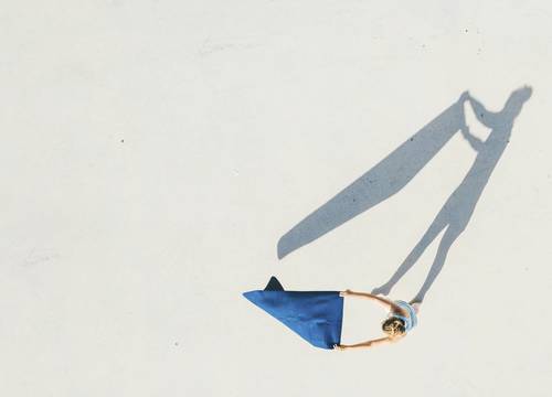 Aerial view of a person on a white surface laying out a blue towel and casting a long shadow.