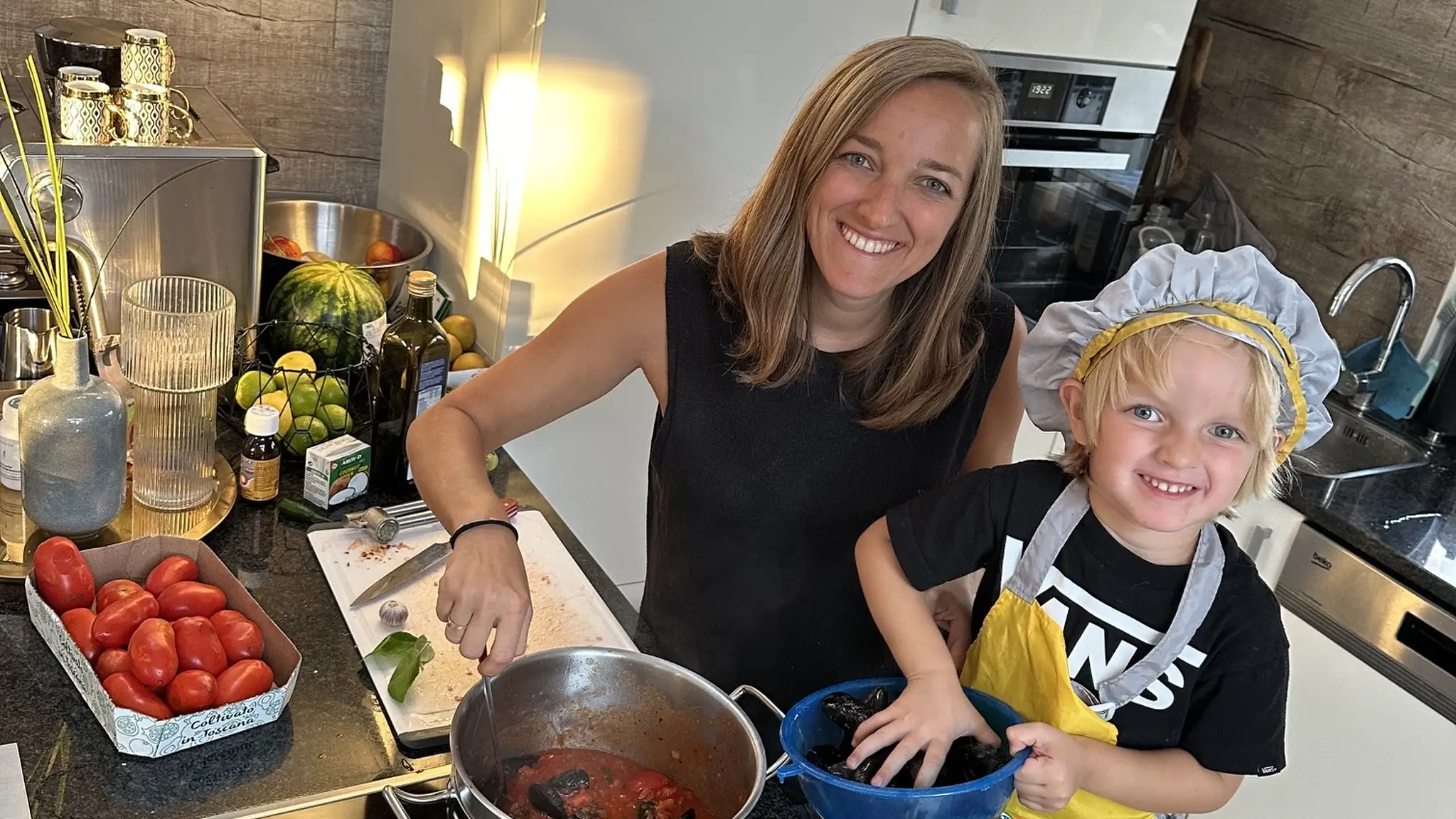 Frau und Kind in Küche beim Kochen mit Tomaten und Muscheln