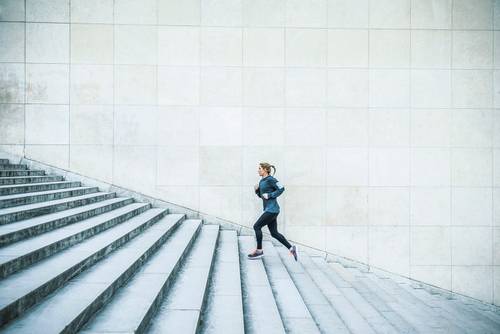 Person in sportswear running up a wide concrete staircase in front of a large tiled wall.