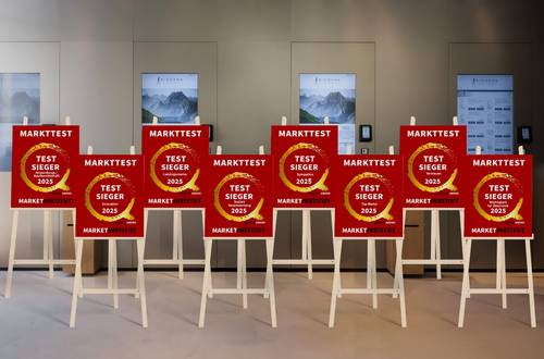 Sieben rote „Test Sieger 2024“-Auszeichnungsschilder auf Ständern sind in einer Reihe aufgestellt, im Hintergrund sind moderne Tafeln zu sehen.