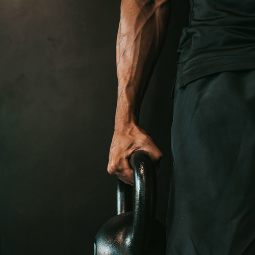 Ein muskulöser Arm, der eine Kettlebell vor einem dunklen Hintergrund hält und Stärke und Fitness symbolisiert.