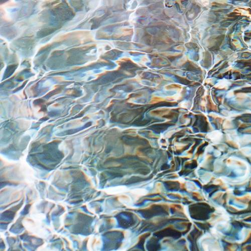 Sonnenlicht, das sich auf kräuselndem Wasser spiegelt, erzeugt ein Muster aus schimmernden, vielfarbigen Wellen.