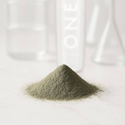 Ein kleiner Hügel aus feinem grünen Pulver auf einer weißen Oberfläche, mit verschwommenen Glasbehältern im Hintergrund.
