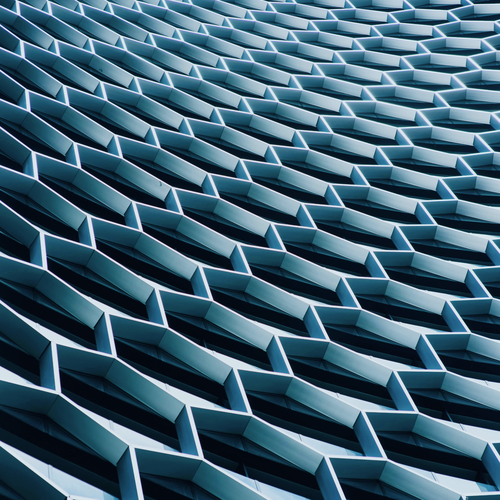 An abstract architectural pattern comprising undulating, overlapping hexagonal shapes, creating a dynamic, flowing surface in shades of blue and grey.