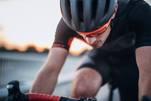 Ein Radfahrer in schwarzer Kleidung und mit Helm fährt intensiv mit dem Sonnenuntergang im Hintergrund und konzentriert sich auf die Straße vor ihm.