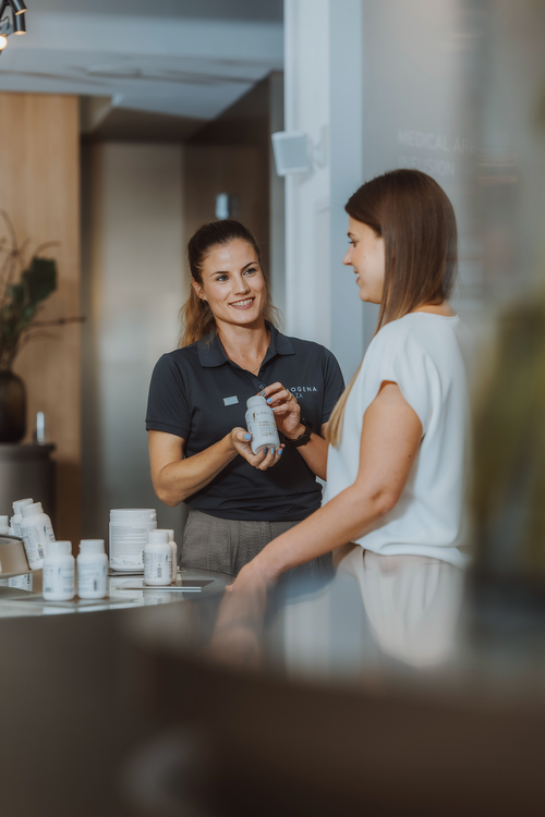 Ein BIOGENA Good Health Coach zeigt einem Kunden ein Produkt in einem hellen Ladenumfeld. Verschiedene Flaschen sind auf dem Tresen ausgestellt.