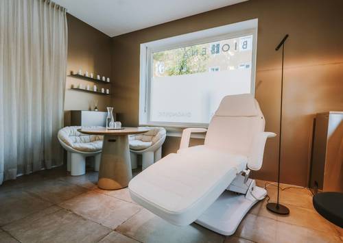 Moderner Wellnessraum mit weißem Liegestuhl, rundem Tisch und gemütlicher Sitzgelegenheit. Sanfte Beleuchtung und neutrale Farbtöne schaffen eine ruhige Atmosphäre.