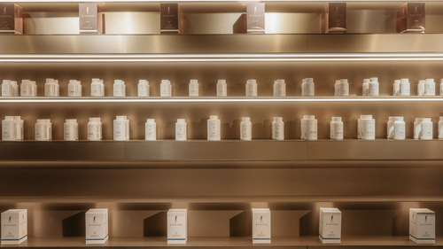Regale, in denen eine Auswahl an BIOGENA-Produkten in weißen Behältern und Schachteln präsentiert wird, vor einem Hintergrund in warmen Farbtönen und bei sanfter Beleuchtung.