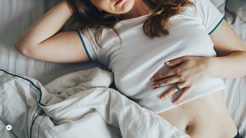 Frau liegt im Bett und hält sich mit der Hand den Bauch bei Magenbeschwerden.