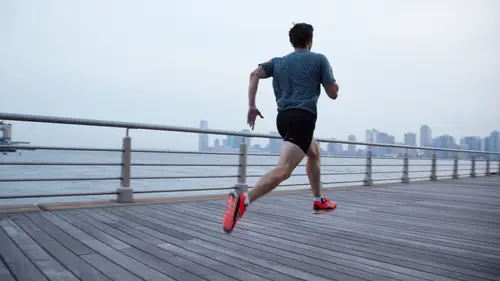 Eine Person, die an einer Uferpromenade entlangläuft, im Hintergrund die Skyline der Stadt.
