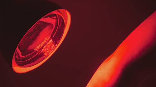 Eine rote Lampe leuchtet auf einen Unterarm und wirft einen intensiven roten Schein vor einem dunklen Hintergrund.