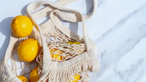 Bolsa de red con limones frescos sobre una superficie de mármol blanco, proyectando sombras suaves.