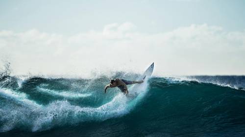 Surfer skillfully riding a large wave under a clear sky, with water splashing around.