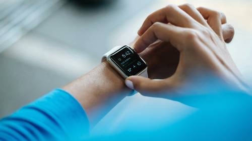 Person interacting with a smartwatch displaying the time and health metrics, wearing a blue shirt.