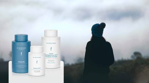A silhouetted person in a beanie looks at a foggy landscape. Three BIOGENA supplement bottles are displayed in the foreground.