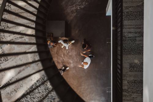 Luftaufnahme von Menschen, die in einem Bereich mit Wendeltreppe gehen, mit Schatten auf dem Boden und einem Geländer, das links zu sehen ist.