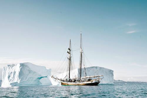 Sailing ship in front of two huge icebergs in calm, blue water under a clear sky.