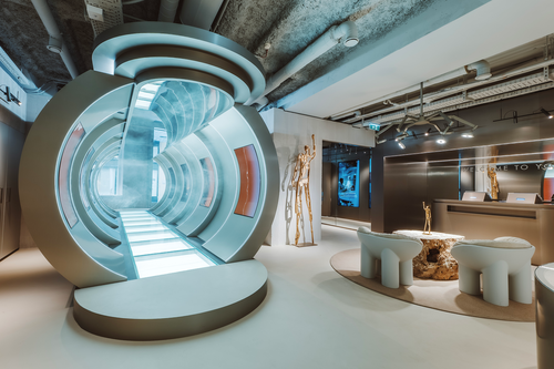 Futuristic interior with a circular glass tunnel, modern seating, and a reception area with metallic and wooden decor under exposed ceilings.