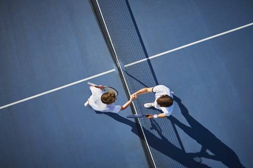 Doi jucători de tenis își strâng mâna peste fileu pe un teren albastru, văzuți de sus.