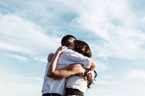 A couple embraces warmly under a clear blue sky, expressing joy and affection.