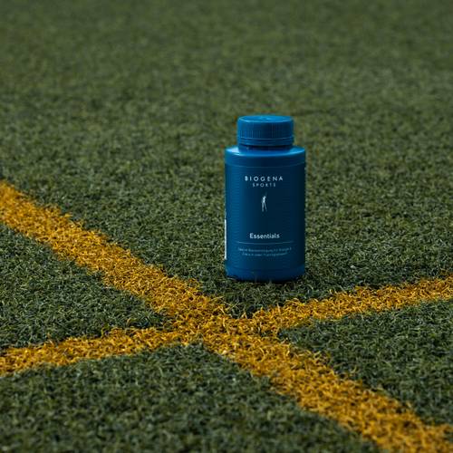 Eine blaue Flasche mit dem Etikett "Biogena Sport Essentials" auf einem grünen Sportplatz mit einer gelben Linienkreuzung.