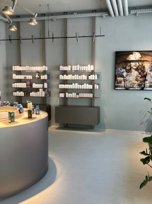 Modernes Ladendesign mit Regalen voller weißer Flaschen, einer geschwungenen Theke mit Produkten und einem großen Kunstwerk an der Wand. Minimalistische Einrichtung.