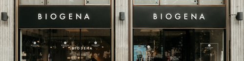 Shop windows with the inscription "BIOGENA" in bold letters, large shop windows with interior lighting and advertising posters.