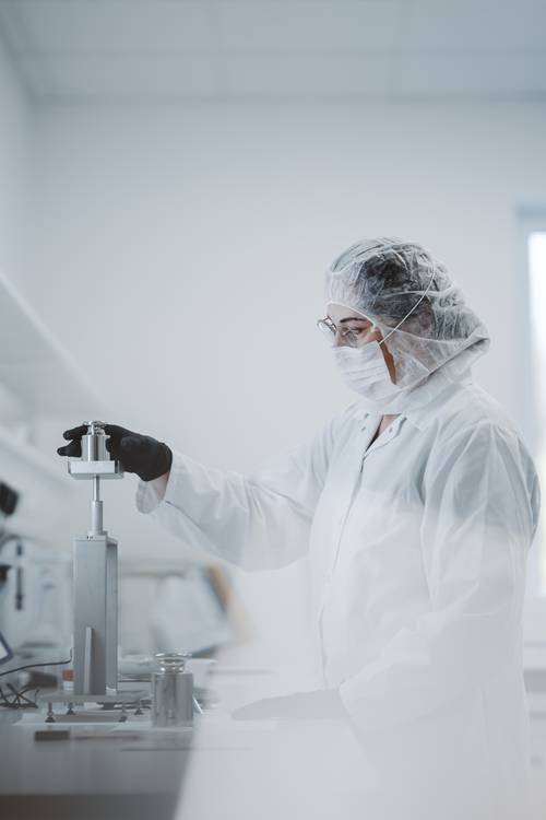 Persoană în îmbrăcăminte de protecție și ochelari de protecție lucrând cu echipamente într-un laborator de producție.
