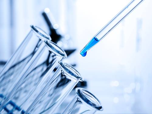 Close-up of a pipette dropping blue liquid into a row of tilted test tubes in a laboratory setting.