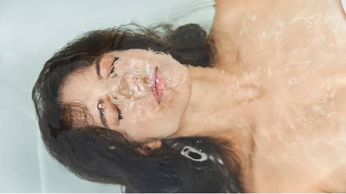 Person with closed eyes floating in clear water, face partially submerged, creating a serene and peaceful atmosphere.