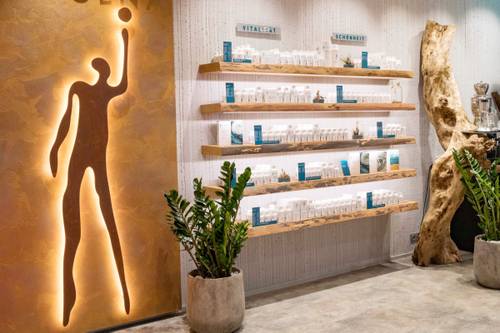 Ein moderner Wellness-Laden mit Holzregalen, auf denen Produkte ausgestellt sind, einer leuchtenden abstrakten Figur an der Wand und Topfpflanzen auf dem Boden.