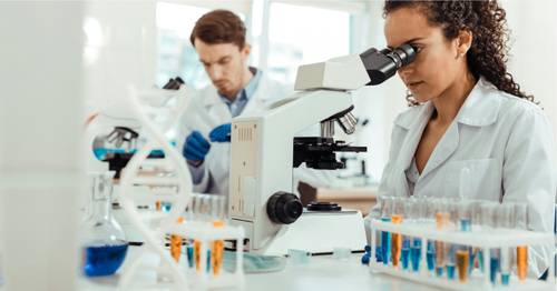 Wissenschaftler in Laborkitteln arbeiten mit Mikroskopen in einem Labor und konzentrieren sich auf Gesundheitsforschung.