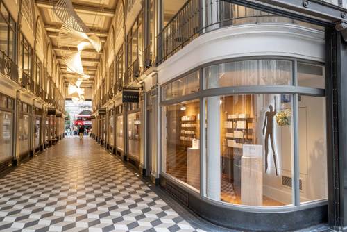 Elegante Einkaufspassage mit geschwungenen Schaufenstern, kariertem Boden und moderner Beleuchtung. In einem Schaufenster ist eine Schaufensterpuppe zu sehen