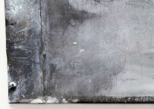 Nahaufnahme einer verwitterten Metalloberfläche mit verschiedenen Grautönen, Kratzern und Strukturen, die Abnutzungs- und Korrosionsspuren aufweist.