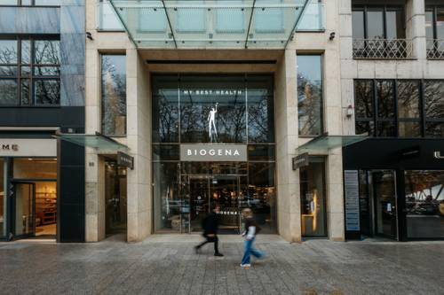 Storefront of BIOGENA Plaza Düsseldorf with glass entrance, modern design, and pedestrians walking by on the street.
