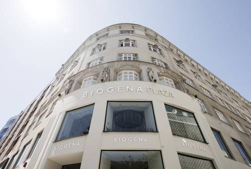 Straßenansicht des BIOGENA Plaza, eines geschwungenen mehrstöckigen Gebäudes mit großen Fenstern und dekorativen Skulpturen unter strahlend blauem Himmel.
