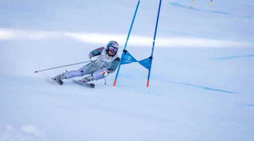 Marcel Hirscher: Un schior în echipament de cursă cu cască RedBull navighează pe un traseu de slalom, înclinat brusc în jurul unei porți albastre pe o pantă acoperită de zăpadă.
