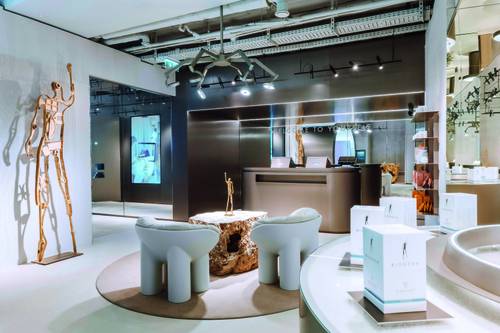 Modernes BIOGENA-Lounge und Ausstellung mit eleganten Möbeln, einer Holzskulptur und ambienter Beleuchtung. Weiße Stühle umgeben einen Holztisch, mit Produkten in der Nähe ausgestellt.