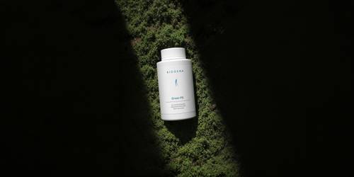A white bottle bearing the inscription ‘GreenPE’ on green moss, illuminated by spotlights against a dark background.