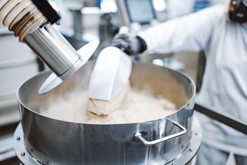 Persoană în echipament de protecție adaugă pudră într-o mașină mare de amestecat în fabrica de producție BIOGENA din Koppl, Austria.