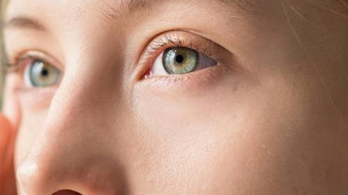 Close-up of a person's face focusing on their light green eyes and smooth skin, with soft lighting highlighting the eye area.