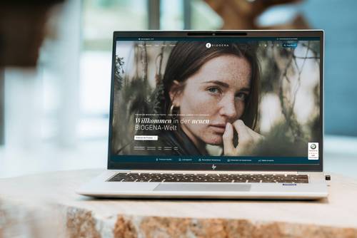 Ein offener Laptop auf einem Holztisch, auf dem eine Webseite mit dem Porträt einer Frau und einem Text auf Deutsch zu sehen ist.