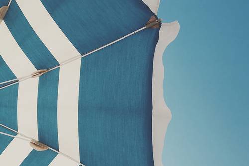 Close-up of a blue and white striped beach umbrella against a clear blue sky, with metal supports visible.