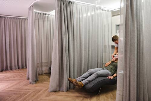 Person, die eine Gesichtsbehandlung in einem Spa-Raum mit grauen Vorhängen und Holzboden erhält.