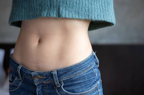 Close-up of a person's upper body wearing blue jeans and a teal sweater, revealing a bare stomach with a visible belly button.