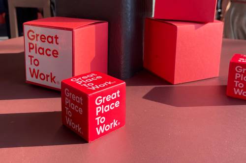 Rote Würfel mit der Aufschrift „Great Place To Work” auf einem Tisch, beleuchtet vom Sonnenlicht.