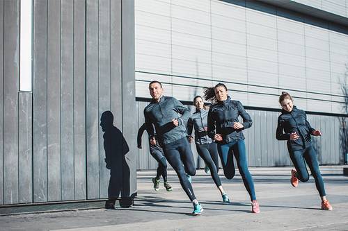 Vier Personen in Sportkleidung laufen energisch vor einem modernen Gebäude und werfen Schatten auf den Boden.