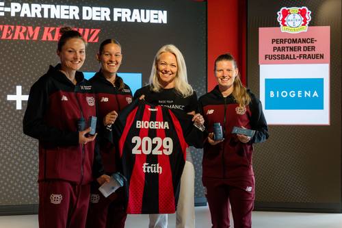 Vier Frauen posieren mit einem BIOGENA 2029-Trikot und lächeln vor einer Kulisse mit einem Logo und Sponsorenlogos.