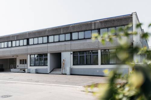 A two-storey industrial building with large windows and a small flight of stairs; there is a sculpture next to the entrance.
