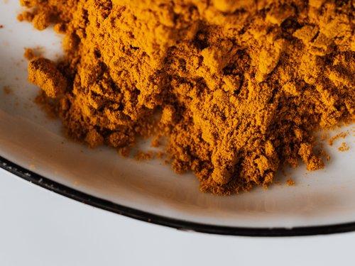 A close-up of bright orange turmeric powder on a white plate with a black rim, showing its fine texture.
